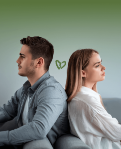 Pareja de un hombre a la izquierda y mujer a la derecha sentada espalda con espalda con un fondo verde y un corazón verde roto que representa el fin de su amor. Ahora les toca averiguar cómo afrontar una ruptura amorosa.