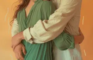 El cuerpo de una chica y el de un chico dándose un cálido abrazo. La chica viste un vestido verde y el chico una camisa blanca larga y ancha. La teoría del apego tiene mucho que decir sobre el amor que esta pareja y todos procesamos.