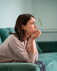 Mujer preocupada sentada en un sofá de terciopelo verde. Mira hacia delante, mientras apoya su cabeza en su mano, está pensativa, asustada. Es posible que piense que su relación está estancada y quizás ha llegado a su fin, es víctima del quiet quitting.