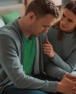 Aparece una pareja de forma seria sentados en el sofá de casa. La mujer esta pidiéndole disculpas al hombre y este esta con la cabeza agachada.