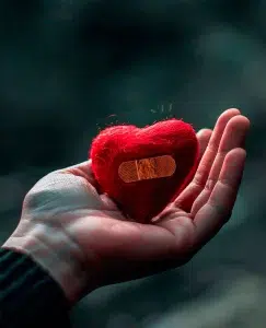 Una mano sosteniendo un corazón con un tirita de forma amable