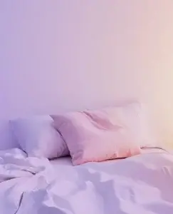 La cama, iluminada por una luz tenue que se desvanece de lila a naranja, está vacía. Las sábanas revueltas y las almohadas, una de ellas de un delicado rosa pálido, sugieren una presencia reciente, pero la ausencia de una persona crea una sensación de vacío. La imagen evoca una profunda sensación de soledad, que puede relacionarse con la herida de abandono y sexualidad.