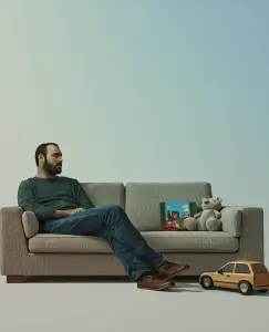 aparece un hombre sentado en el sofá con juguetes al lado ya que antepone a sus hijos