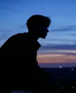 Imagen de un chico en lo alto de un monte mirando pensativo el horizonte en el crepúsculo. Está pensando si seguir o no, ya que ha sufrido una infidelidad en su pareja y ahora es él quien tiene que tomar la decisión.