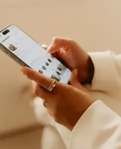 Una persona sostiene un móvil y revisa cuidadosamente perfiles y fotos en redes sociales, con los dedos preparados para deslizar por la pantalla. La escena refleja la inquietud y la comparación constante que puede despertar el síndrome de Rebeca, cuando el pasado de la pareja se convierte en una fuente de dudas e inseguridades.