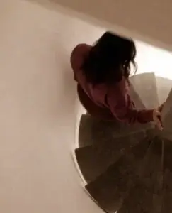 Persona descendiendo por una escalera en espiral con el cuerpo inclinado y gesto de tensión, una imagen que simboliza los celos patológicos como una espiral emocional de pensamientos obsesivos, desconfianza constante y pérdida progresiva de equilibrio afectivo.