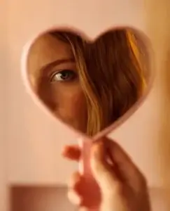 Rostro reflejado parcialmente en un espejo con forma de corazón, una imagen que simboliza a una persona ególatra centrada en su propia imagen, validación y autoimportancia emocional.
