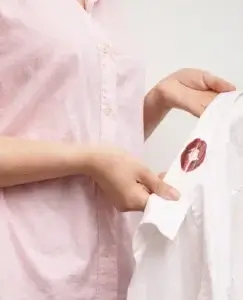 Una persona sostiene una camisa blanca con una marca de labios rojos en el cuello, una escena simbólica que evoca la traición y el impacto emocional detrás de reflexionar sobre 5 razones para no perdonar una infidelidad.