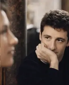 Un hombre observa con atención a una mujer mientras apoya la cabeza en su mano, una mirada discreta pero cargada de interés que refleja las señales de que le gustas pero no lo admite.