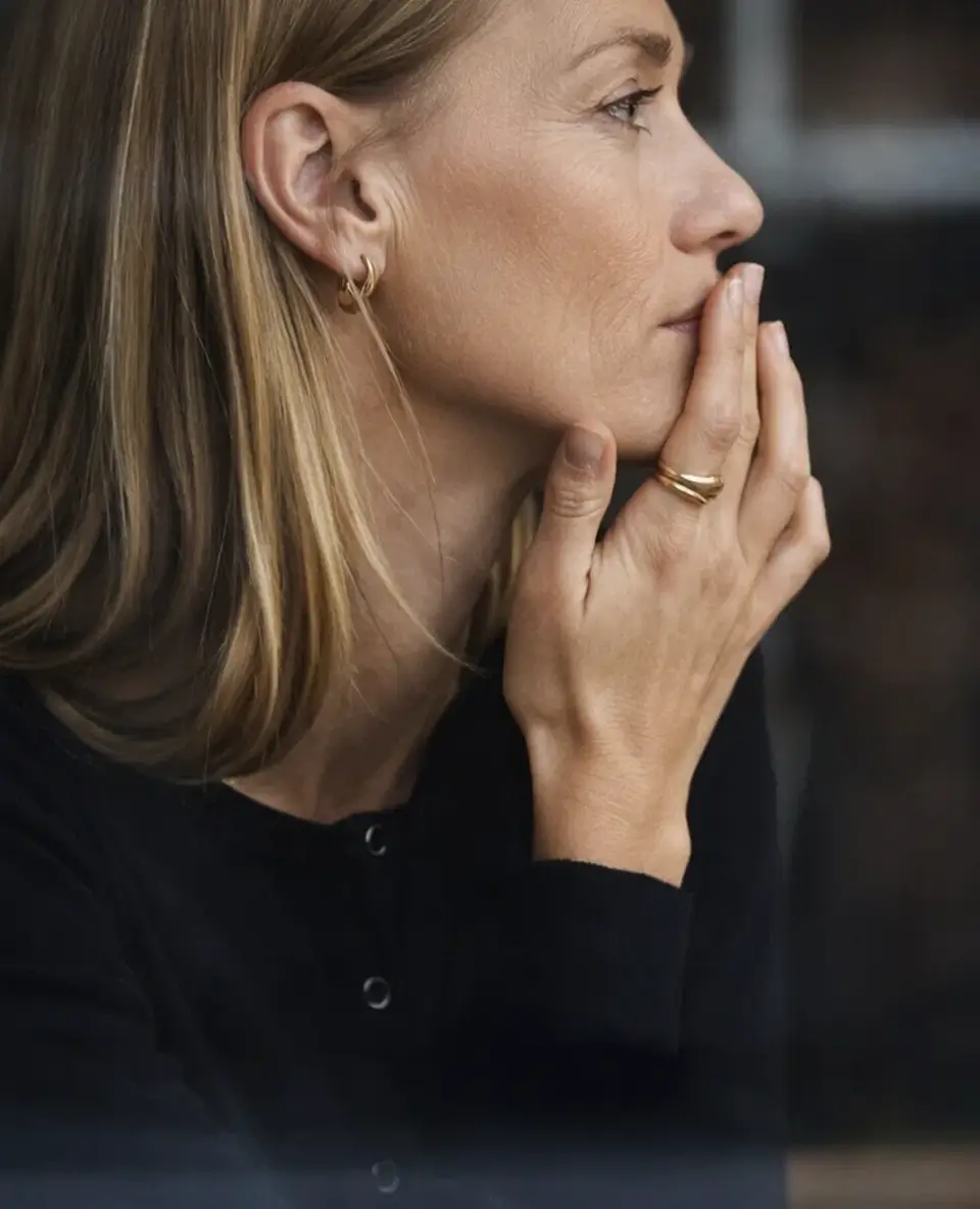 Una mujer mira hacia la distancia con gesto pensativo mientras apoya la mano en el rostro, una escena que refleja la introspección y las emociones profundas asociadas a separarse a los 40, lo que nadie te cuenta.