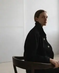 Una mujer sentada en una silla gira ligeramente la cabeza con una mirada serena pero firme, transmitiendo determinación y autocontrol, una imagen que simboliza la actitud necesaria cuando te planteas si el narcisista vuelve, aplicar estos 7 puntos para proteger tu bienestar emocional.